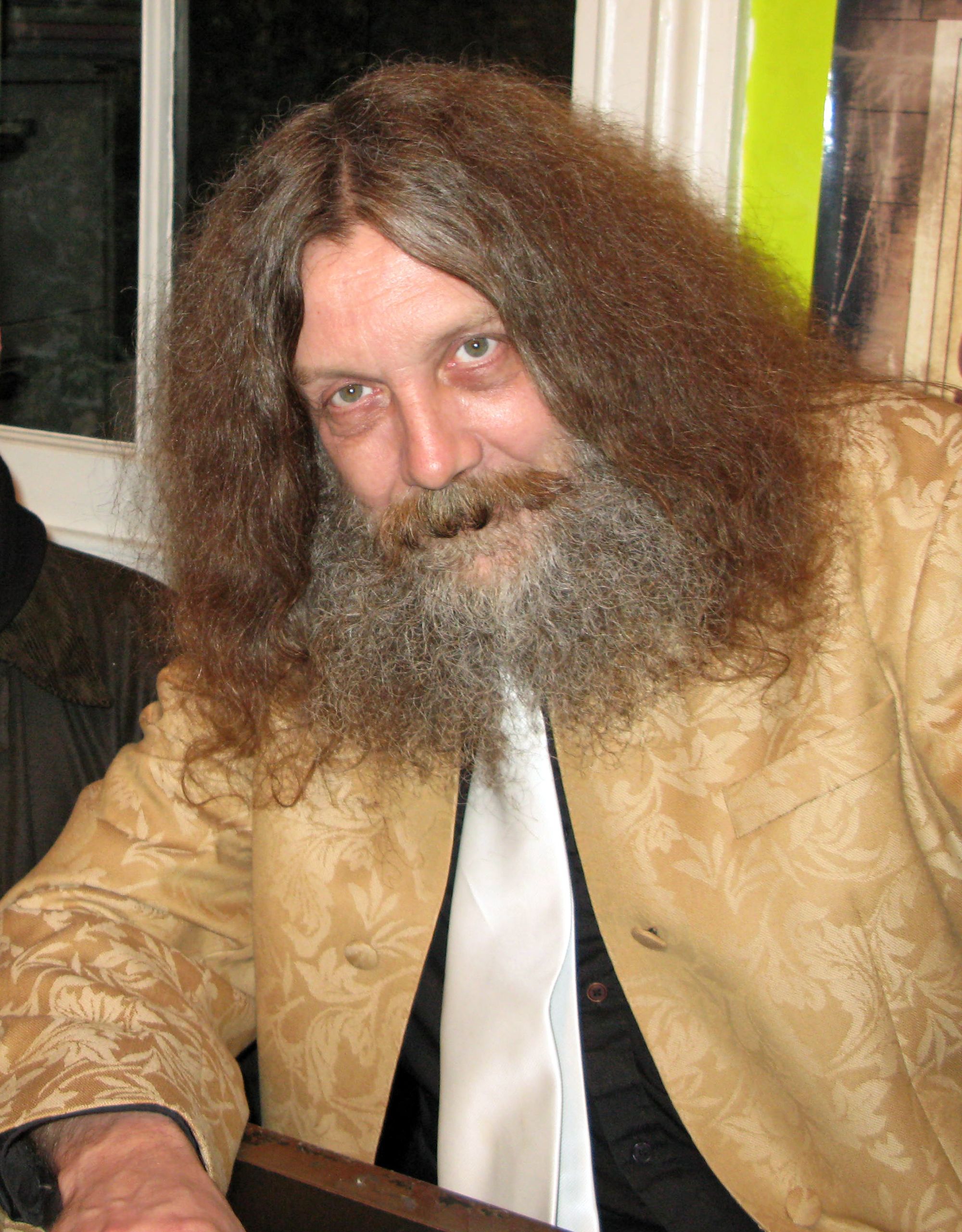 A bearded man wearing a beige jacket.