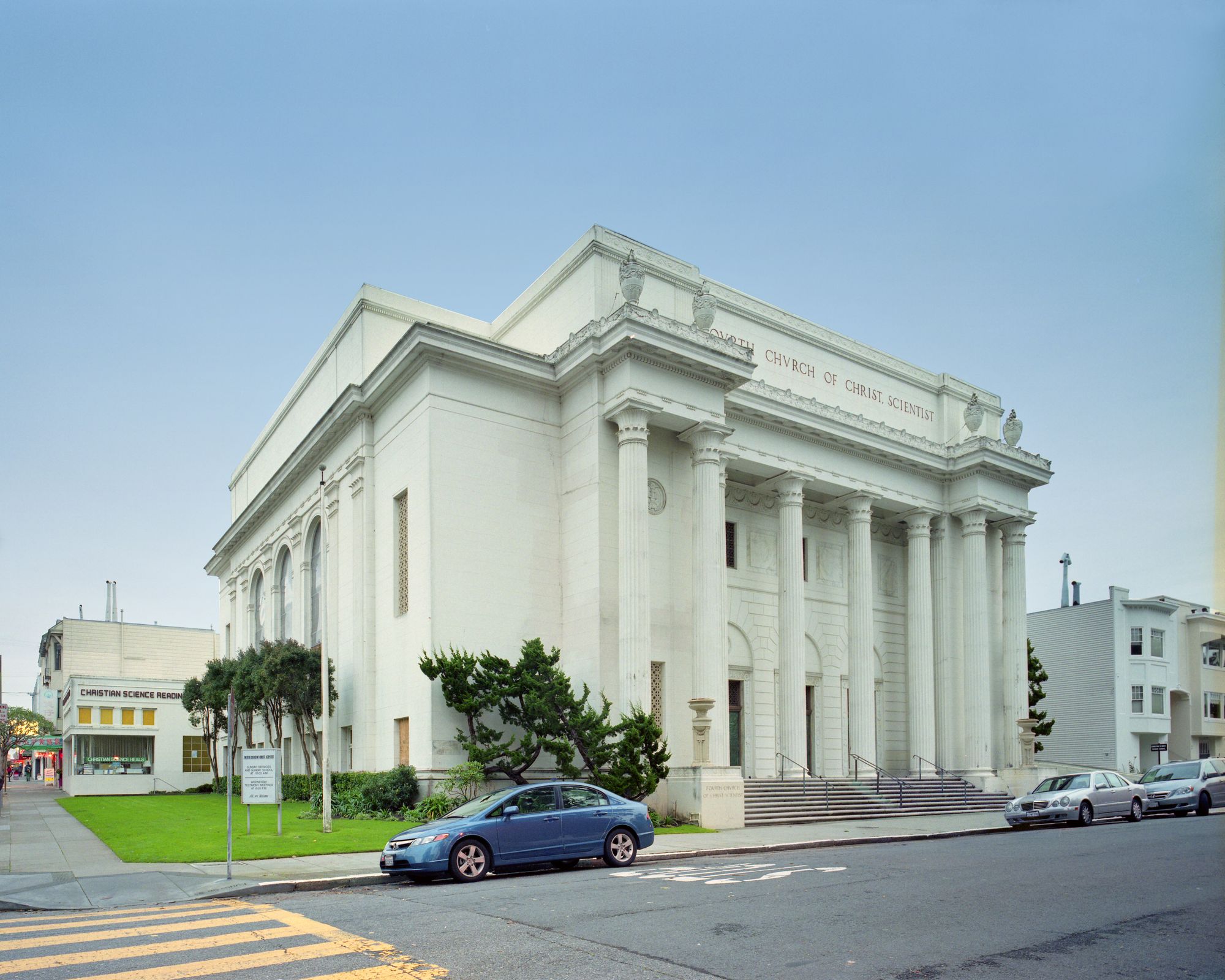 A white neoclassical building with some cars parked in front.