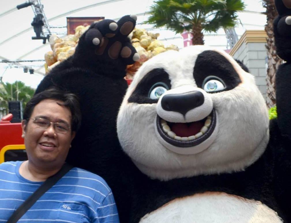 A man in a blue shirt taking a selfie with someone in a panda costume.