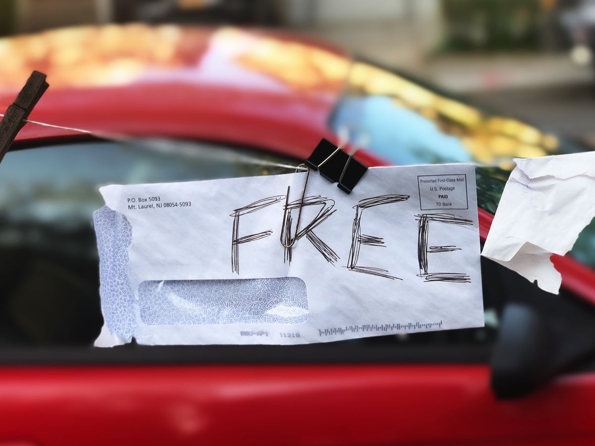 An envelope with the word FREE written on it, attached to a red car.